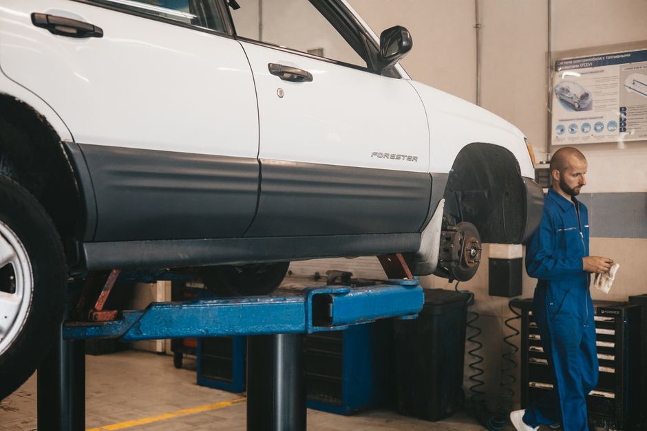 Mechanic evaluating a car on a lift for maintenance in an auto workshop.