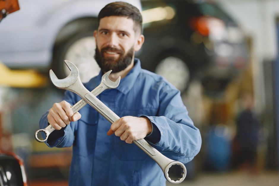 Mechanic in blue uniform holding wrenches inside an auto repair shop, ready for vehicle maintenance.